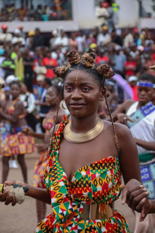 A woman dancing in kente-pattern dress and gold jewellery