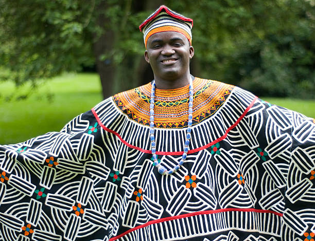 A man smiling in a traditional patterned robe and cap