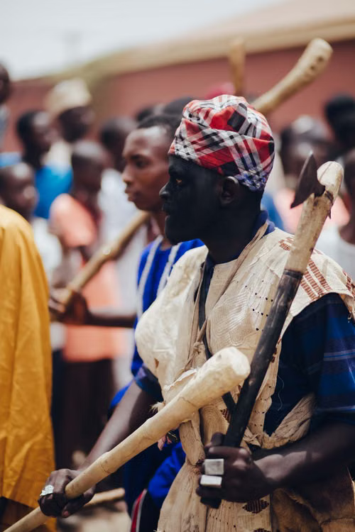 A man in masquerade dress holding ceremonial staffs